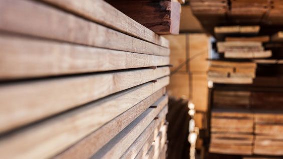 Des planches de bois empilées, alignées horizontalement, dans un environnement de stockage lumineux.