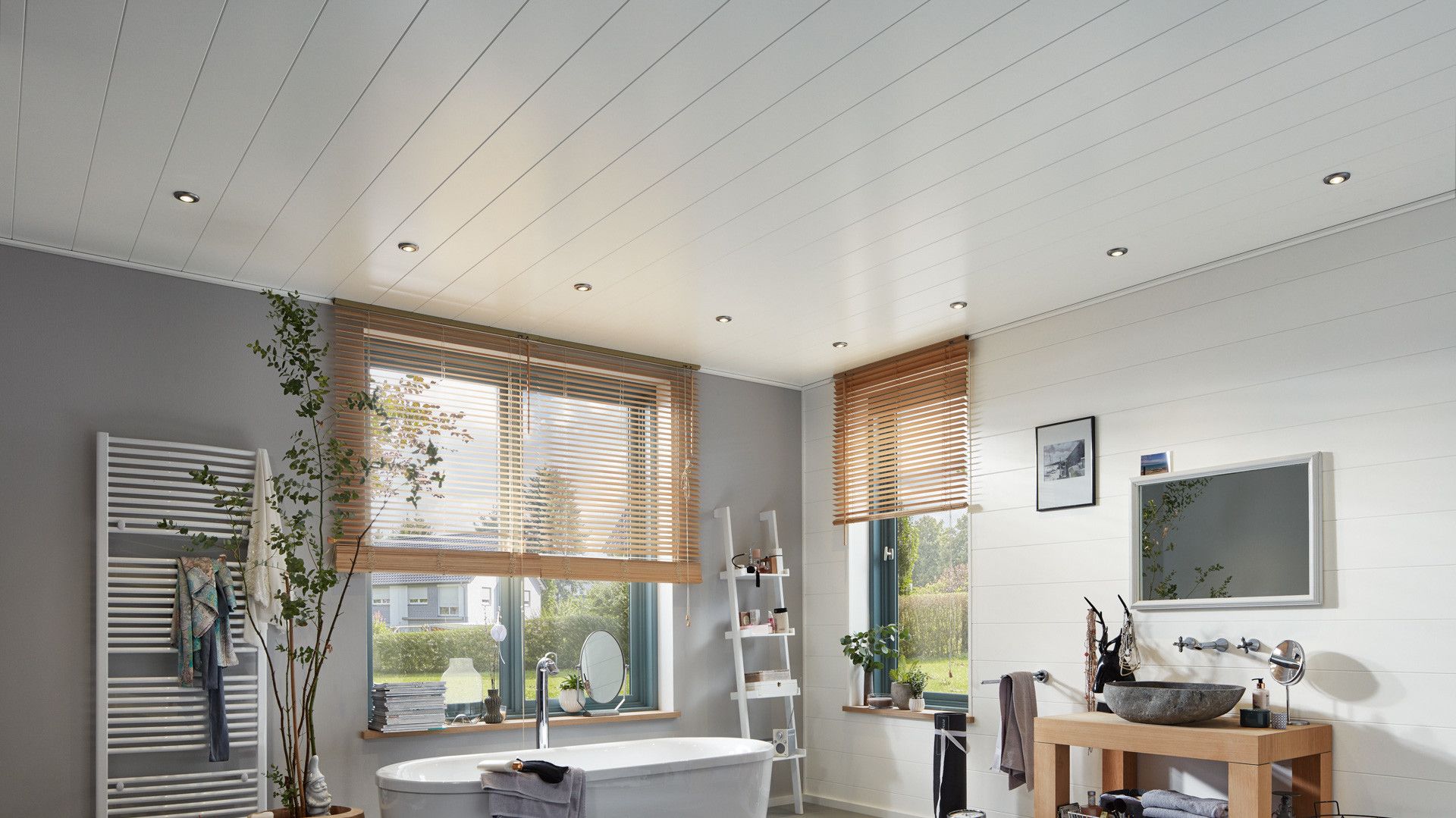 Salle de bain moderne avec baignoire, plantes, fenêtres, et éclairage encastré. Ambiance lumineuse et aérée.
