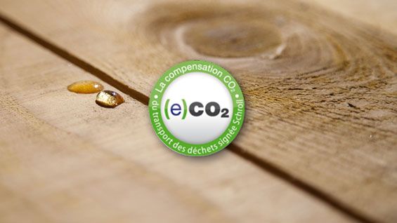 Gouttes d'eau sur une surface en bois, avec un logo sur la compensation CO₂ au centre.