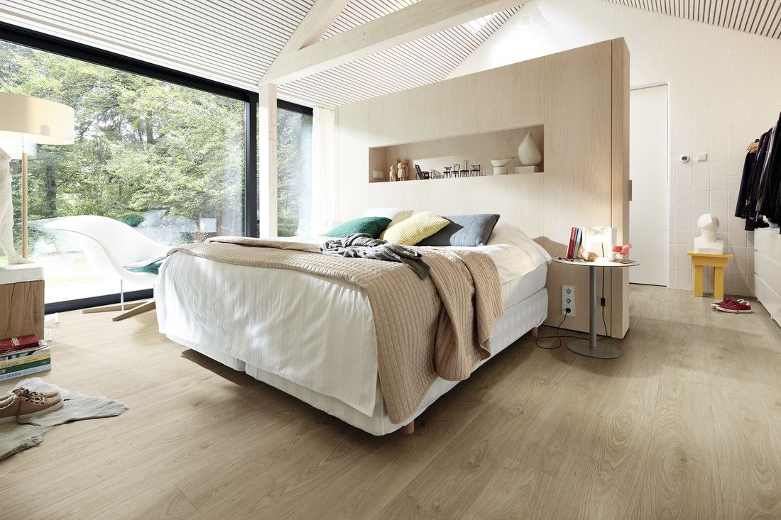 Chambre moderne avec un lit, des coussins colorés et une grande fenêtre donnant sur l'extérieur.