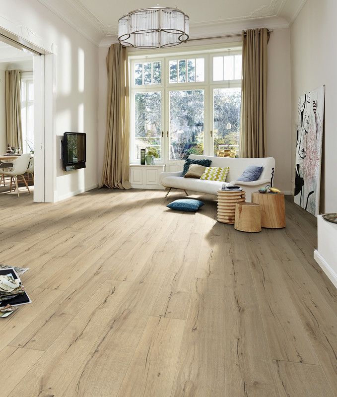 Salon lumineux avec un canapé, des coussins colorés, un sol en bois et de grandes fenêtres.