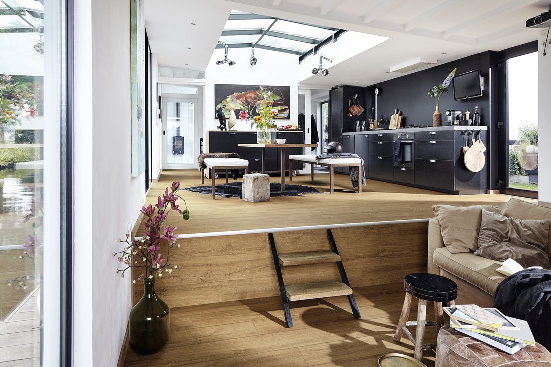 Espace de vie moderne avec cuisine, table, plantes et escaliers, lumineux et accueillant.