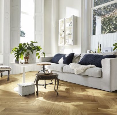 Salon lumineux avec un canapé blanc, des plantes, une table basse et un parquet en bois.