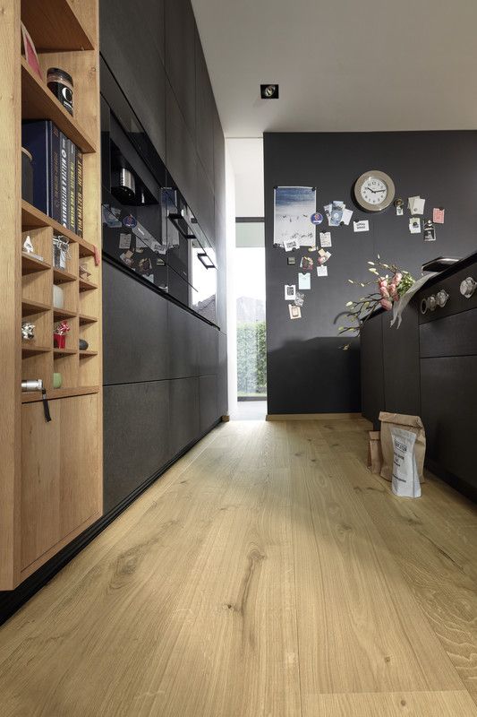 Cuisine moderne avec un sol en bois, meubles noirs, et un mur décoré de photos.