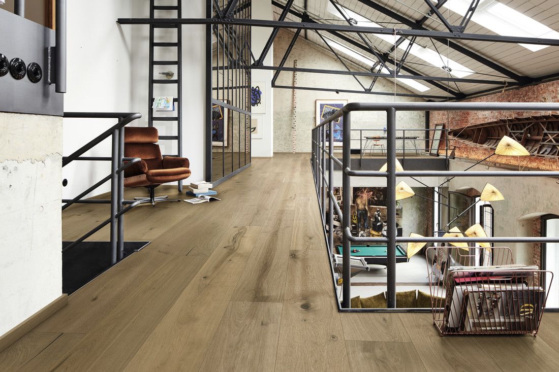 Espace intérieur moderne avec un sol en bois, un fauteuil et une mezzanine visible.