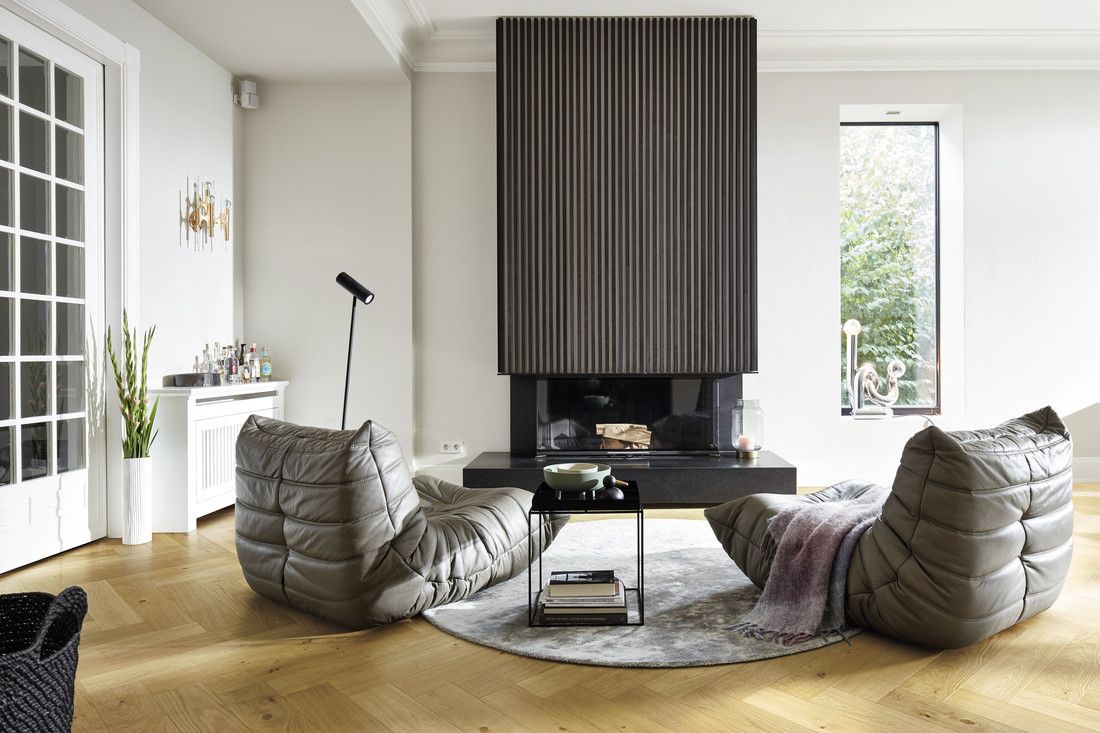 Espace de vie moderne avec fauteuils confortables, table basse, cheminée et lumière naturelle.