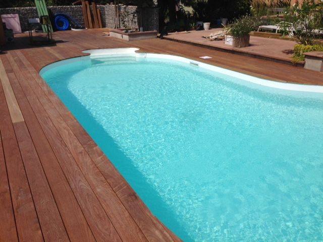 Piscine turquoise entourée de bois, reflétant le soleil, dans un jardin verdoyant.