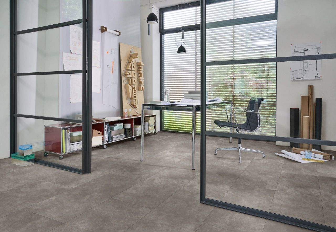 Bureau moderne avec un bureau en verre, des documents, et des étagères, baigné de lumière naturelle.