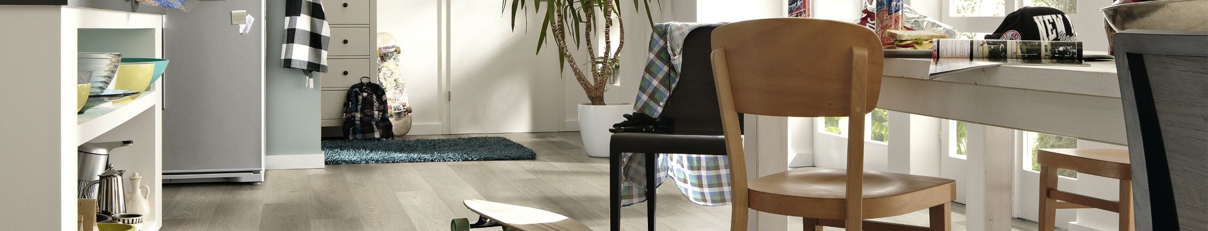 Chaises en bois et table, skateboard au sol, désordre léger dans un intérieur lumineux.