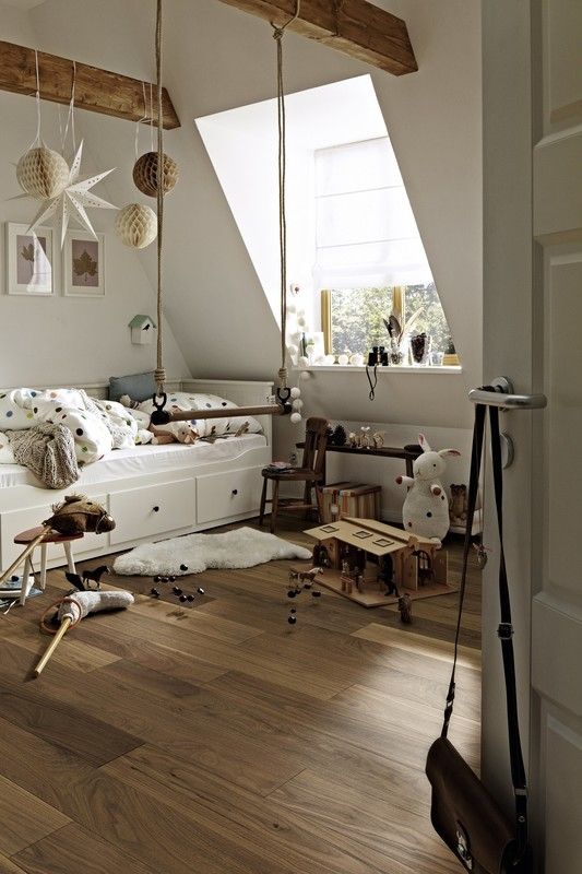 Chambre d'enfant avec lit, jouets éparpillés, et décorations suspendues au plafond. Ambiance chaleureuse.