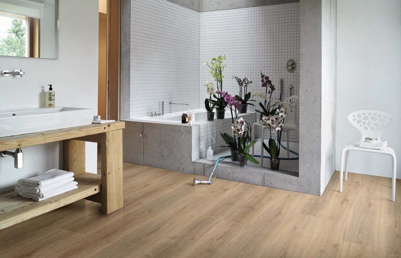 Salle de bain moderne avec baignoire, plantes fleuries, meuble en bois et sol en bois clair.