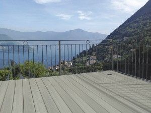 Terrasse en bois avec balustrade, offrant une vue panoramique sur un lac et des montagnes.