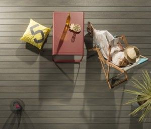 Tableau avec une chaise, un livre, un coussin décoratif et une plante sur un sol en bois.