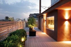 Terrasse moderne avec éclairage doux, plantes en pot et vue sur la ville au crépuscule.